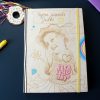 Zdjęcie przedstawia notes personalizowany dla nastolatki - "Tajne zapiski Julki" . Okładka przedstawia właścicielkę notesu - uśmiechniętą dziewczynkę w kapeluszu, pewne elementy są kolorowe, a pozostałe to klasyczne drewno. W górnej części obrazka widzimy także brelok przedstawiający donata z kolorową posypką i frędzlami nawiązującymi do kolorowych elementów na okładce.